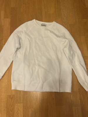 Vit sweatshirt från Acne Studios - Säljer en stilren vit sweatshirt från Acne Studios. Tröjan har rund halsringning, långa ärmar och ribbade muddar vid hals, ärmslut och nederkant. Perfekt basplagg för en clean och modern look.