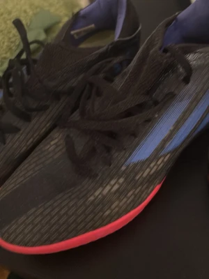 Svarta löparskor med blå detaljer - Säljer ett par snygga inneskor i svart med blåa detaljer och rosa sula. Skorna har en sportig design med mesh-ovandel för bra ventilation och snörning för optimal passform. Perfekta för dig som gillar att springa snabbt och vill ha stilrena skor.