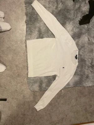 Vit långärmad tröja från Ralph Lauren - Klassisk vit långärmad tröja från Ralph Lauren med rund halsringning och den ikoniska svarta polospelaren broderad på bröstet. Tröjan är i mjukt material och har en stilren, enkel design som passar till det mesta.