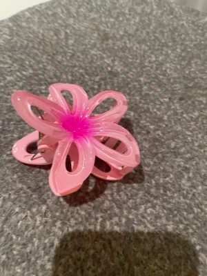 Rosa blomformad hårklämma - Säljer en rosa hårklämma i form av en blomma med öppna kronblad och en intensiv rosa mitt. Klämman är tillverkad i plast och är perfekt för dig som vill ha en mer somrig och färgglad look.
