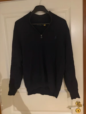 Mörkblå halvzip från Polo Ralph Lauren - Säljer en mörkblå stickad tröja från Polo Ralph Lauren med halv dragkedja och diskret logga på bröstet. Tröjan har ett skönt material och funkar perfekt i vardagen. Nypris på tröjan är en bit över 2000 så tycker 450 är ett bra pris