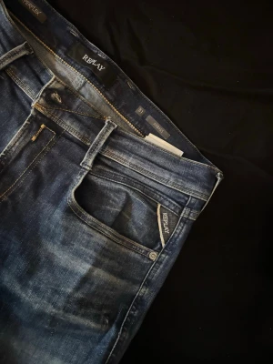 Mörkblå Replay jeans med slitningar - Snygga mörkblå jeans från Replay med diskreta slitningar och klassisk femficksdesign. Jeansen har en slim fit-passform och detaljerade sömmar på bakfickan. Perfekta för en trendig och avslappnad look.