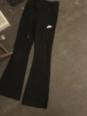 Svarta bootcut leggings från Nike - Snygga svarta leggings från Nike med bootcut-modell och vit logga på låret. Stretchigt material som sitter skönt och följer kroppen. Perfekta till både chill och träning. Klassisk och enkel design som passar till det mesta.