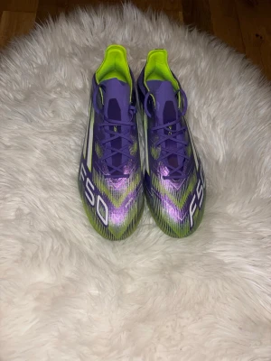 Adidas F50 lila och gröna fotbollsskor - Säljer ett par Adidas F50 fotbollsskor i en riktigt snygg lila och grön färgkombination med vita detaljer. Skorna har en låg profil, snörning och ovandel i syntetmaterial för lätt vikt och bra bollkontroll. Perfekta för dig som vill sticka ut på planen!.skorna är dessutom aldrig använda och priset kan diskuteras 