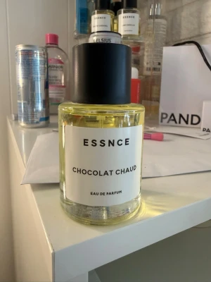 ESSNCE Chocolat Chaud Eau de Parfum - Parfymflaska från ESSNCE med doften Chocolat Chaud. Flaskan är rund och genomskinlig med svart lock och vit etikett med svart text. Innehållet är ljusgult. Perfekt för dig som gillar varma, chokladiga doftnoter. Testad 1 gång!
