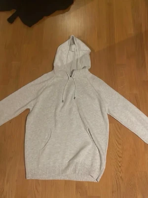 Ljusgrå hoodie med huva - En stilren ljusgrå hoodie med huva och dragsko. Hoodien har en klassisk känguruficka framtill och ribbade muddar vid ärmslut och nederkant. Perfekt för en avslappnad och casual look. Materialet känns mjukt och bekvämt, troligen bomullsblandning.