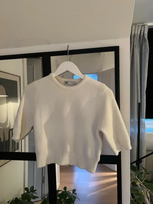 Vit stickad Zara  - En vit stickad tröja från Zara med korta ärmar, cropped passform och rund halsringning. Den är sparsamt använd och i fint skick. I storlek S men passar även Xs om man vill ha den lite längre! 