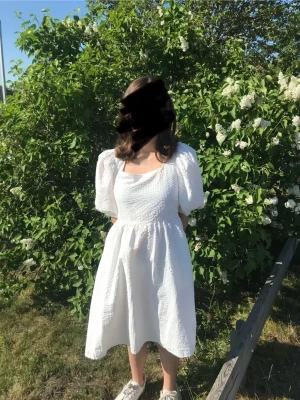 Vit puffärmad klänning med knyt - Söt vit klänning med puffärmar och fyrkantig ringning. Klänningen har struktur i tyget, knyt i ryggen och en luftig passform som ger en romantisk känsla. Perfekt för varma dagar och somriga tillfällen.