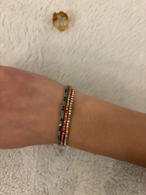 3 färgglada armband  - Säljer ett armband med flera tunna rader av små pärlor i olika färger som turkos, röd, vit och gul. Armbandet har en enkel och trendig design som passar perfekt till din vardagsstil. Materialet är pärlor trädda på elastisk tråd. Inte jätte bra kvalitet så vill sälja billigt