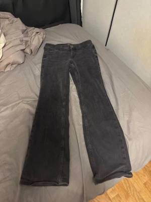 Svarta bootcut jeans från Lee - Snygga svarta bootcut jeans från Lee med klassisk femficksdesign och dragkedjegylf. Jeansen har en lätt utsvängd passform nertill och är tillverkade i ett mjukt denimtyg. Perfekta för dig som gillar en retrostil med modern twist.