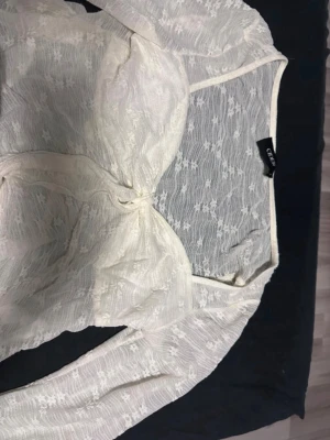 Vit spetsblus från Cider - Säljer en vit spetsblus från cider med långärmad design. Blusen har transparent spetsmaterial med blommönster och en knytning framtill. Perfekt för dig som gillar romantisk och trendig stil. Den är ganska noppig som man ser på bilderna. Står L men passar bättre som M 