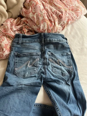 Blå jeans med detaljer från Nelly - Snygga blå jeans från Nelly med raka ben och coola vita sömdetaljer på bakfickorna. Jeansen har dubbla knappar i midjan och klassisk femficksdesign. Perfekta för dig som vill ha ett par trendiga och bekväma jeans i garderoben.