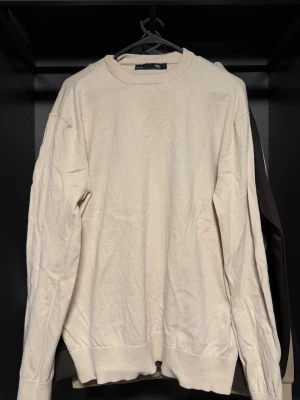 Beige basic tröja från H&M - En enkel beige tröja från H&M med rund halsringning och långa ärmar. Tillverkad i mjukt material, perfekt för lager på lager och en clean look. Ribbstickade muddar vid ärmslut och nederkant.