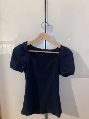 Mörkblå ribbad topp med puffärm - Trendig mörkblå topp med puffärmar och fyrkantig ringning. Toppen är ribbad och har en figurnära passform som ger en snygg siluett. Perfekt att styla med jeans eller kjol för en cool look.