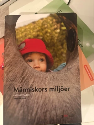 Människors miljöer kursbok - Kurslitteratur 'Människors miljöer' av Tove Phillips, andra upplagan. Boken har ett färgstarkt omslag med naturmotiv och en person i röd jacka. Perfekt för studier inom pedagogik och samhälle.