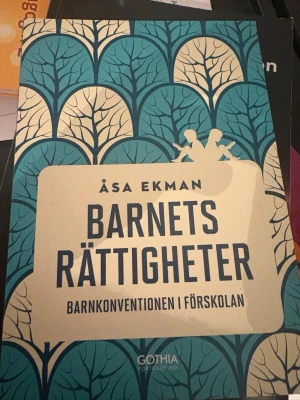 Barnets rättigheter kursbok - Kurslitteratur med titeln 'Barnets rättigheter: Barnkonventionen i förskolan' av Åsa Ekman. Boken har ett omslag i blått och beige med grafiskt trädmönster och siluetter av barn. Perfekt för dig som pluggar pedagogik eller jobbar inom förskola.