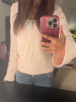 Ljusrosa tröja från Gina tricot - Supersöt ljusrosa stickad omlott-tröja med knytband i sidan, tröjan har långa ärmar och är perfekta att matcha med jeans för en chill look. Änvänd en gång innan.💗