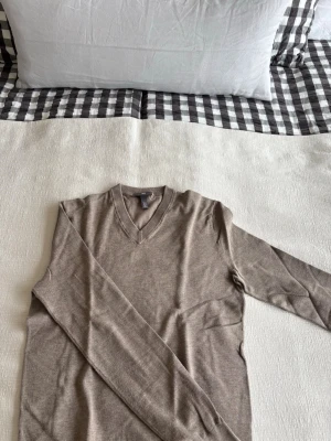 Beige V-ringad stickad tröja H&M - Snygg beige stickad tröja från H&M i slim fit-modell. Tröjan har V-ringning och långa ärmar, perfekt för lager på lager. Tillverkad i mjukt material som känns skönt mot huden. Enkel och stilren design som passar till det mesta.