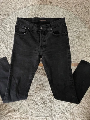 Nudie Jeans Grim Tim - Nudie Jeans Grim Tim  Klassiska svarta jeans från Nudie i mycket bra skick. Storlek: 32/34  Skick: 8/10 inga skavanker såsom hån eller fläckar.    Mått: •Midja: 41cm •Ytterben: 101cm •Innerben: 73cm  Skriv vid intresse!