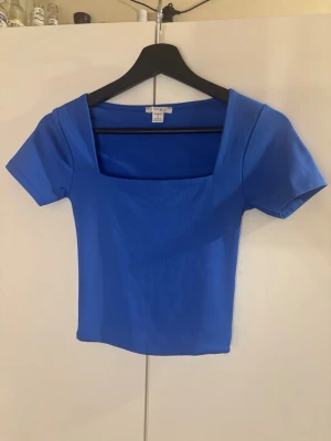 Blå topp med fyrkantig ringning Amisu - En blå topp från New Yorker med korta ärmar och fyrkantig ringning. Modellen är croppad och har en tight passform som framhäver figuren. Perfekt att matcha med höga jeans eller kjol för en trendig look. Andvänt ett antal gånger men fortfarande i väldigt bra skick. Säljer då den inte kommer till användning💕