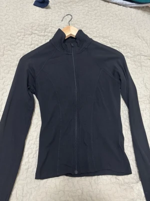 Svart tunn jacka med dragkedja - Snygg svart tunn jacka med hel dragkedja framtill och hög krage. Jackan har lång ärm och en kroppsnära passform, perfekt för lager på lager eller som lättare ytterplagg. Enkel och stilren design utan synliga loggor.