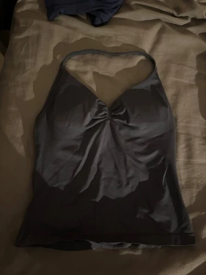 Mörkgrått sportlinne från DFYNE - Snyggt mörkgrått sportlinne från DFYNE med smala axelband och lätt rynkning vid bysten. Tillverkat i stretchigt funktionsmaterial som andas, perfekt för gymmet eller träning. Logga på bröstet och figurnära passform.