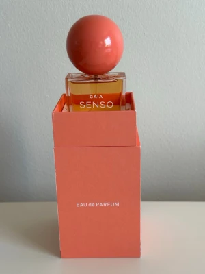 CAIA SENSO Eau de Parfum 50ml - CAIA SENSO Eau de Parfum 50ml i en elegant glasflaska med en stor, rund, korallfärgad kork. Flaskan har en modern och stilren design och kommer i en matchande korallfärgad förpackning. Perfekt för dig som gillar snygga detaljer på parfymhyllan. Säljs inte längre, aldrig använd 🧡