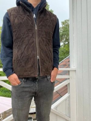 Massimo dutti väst - Säljer en mörkbrun väst i mocka material med två dragkedjor framtill och ståkrage. Västen har ett stilrent rutmönster och passar perfekt över en hoodie eller tröja för en avslappnad look. Brun snygg färg.