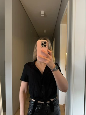 Svart knytblus från Divided - Snygg svart blus från H&M Divided med korta ärmar och knytning framtill. Blusen har klassisk krage och knappar hela vägen ner.