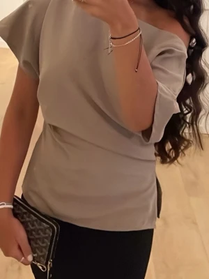 Beige offshoulder topp - Snygg beige topp med offshoulder-design och korta ärmar. Toppens stilrena look gör den enkel att matcha med olika outfits. Materialet känns mjukt och följsamt mot huden.