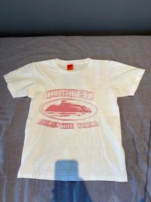 CORTEIZ t-shirt  - Vit t-shirt med rund hals och korta ärmar. Framsidan har ett stort rosa tryck med texten 'Cortez' och grafiskt motiv. Tillverkad i mjuk bomull som känns skön mot huden. Perfekt för dig som gillar en enkel men ändå unik stil.