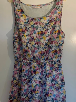 Blommig ärmlös sommarklänning - Söt ärmlös klänning från KIDS ONLY med blommigt mönster i färgerna gul, rosa, blå och vit. Klänningen har rund halsringning och resår i midjan för en bekväm passform. Perfekt för varma dagar och har en lätt, luftig känsla.