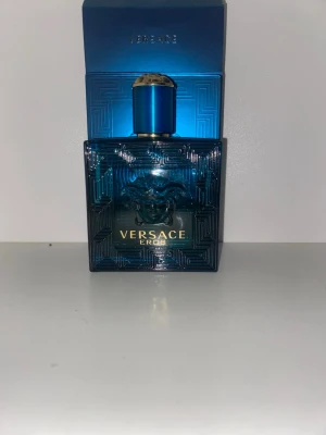Versace Eros parfym blå flaska - Versace Eros parfym i en snygg, fyrkantig blå glasflaska med gulddetaljer och Medusa-huvud på framsidan. Flaskan har ett elegant mönster och ett matchande blått lock med guldfärgad topp. Kommer med originalkartong. Ungefär 60-65% kvar 