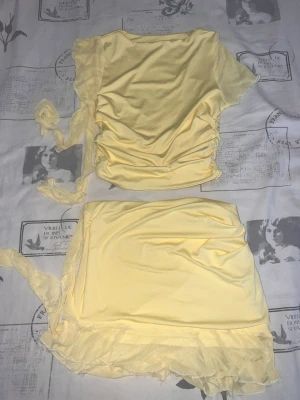 Gul croppad topp med band - Söt ljusgul croppad topp med korta ärmar och band på sidorna. Toppen har en lätt rynkad effekt och meshvolang längst ner. Perfekt för dig som gillar en feminin och trendig stil. Materialet känns mjukt och stretchigt, troligen polyester.