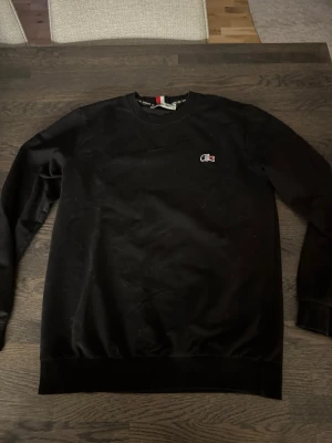 Lacoste sweatshirt - En svart sweatshirt med rund hals och liten broderad logga på bröstet. Tröjan har långa ärmar och ribbade muddar vid ärmslut och nederkant. Perfekt för en avslappnad och stilren look. PASSAR S OCKSÅ