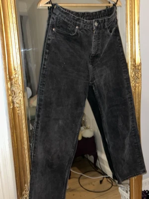 Svarta raka jeans med hög midja - Säljer ett par svarta jeans med rak passform och hög midja. Jeansen har klassiska fem fickor, bälteshällor och knappgylf. Materialet är denim i bomull och färgen har en lätt tvättad look för en cool vibe.