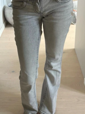 Grå bootcut jeans från True Religion - Säljer ett par gråa bootcut jeans från True Religion med snygga detaljerade bakfickor och knappstängning. Jeansen har en klassisk femficksmodell och är tillverkade i stretchigt denimtyg för skön passform. Perfekta för dig som gillar en avslappnad men trendig look.