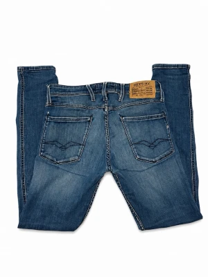 Replay anbass jeans  - Snygga blå slim fit jeans från Replay med klassiska fem fickor, ljusa slitningar och kontrastsömmar. Jeansen har läderpatch med logga bak och detaljerade bakfickor. Perfekta för en trendig och avslappnad look. W28 L30