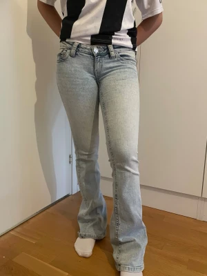 Ljusblå bootcut jeans - Snygga ljusblå bootcut jeans med klassisk femficksmodell och låg midja. Jeansen har en lätt tvättad look och utsvängda ben, perfekta för en trendig och avslappnad stil. Passar dig som gillar retrovibbar och vill ha ett par jeans som sticker ut. Lite slits och smuts längst ner vid bakre foten 