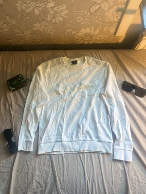 Vit sweatshirt från Hugo Boss - Säljer en stilren vit sweatshirt från Hugo Boss med stort BOSS-tryck framtill. Tröjan har rund halsringning, långa ärmar och ribbade muddar vid ärmslut och nederkant. Tillverkad i mjukt bomullsmaterial för en skön känsla. Kan gå ner något i pris vid en riktigt snabb och smidig affär! 