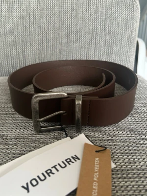 Brunt bälte från YOURTURN - Completely new! Tried it on once at home but it was too big for me & Not real leather. Entire length of the belt: Ca 112cm Hole one: Ca 103cm Hole five: Ca 93cm PS: The belt buckle looks kind of used and a bit dirty but that's just the design, it is completely new and not used at all. If you look it up on Zalando it looks the same there.