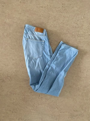 Ljusblå raka jeans - Säljer ett par ljusblå jeans med rak passform och klassisk femficksdesign. Jeansen har en brun patch bak i midjan och är tillverkade i mjuk denim. Perfekta för en avslappnad och trendig look. OBS ett litet märke på framsidan (se bild)