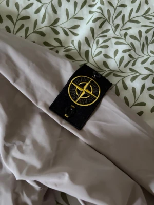 Beige vindjacka från Stone Island - Säljer en beige vindjacka från Stone Island i storlek M. Jackan har dragkedja framtill, huva och den klassiska Stone Island-loggan på ärmen. Materialet är lätt och vindtätt, perfekt för blåsiga dagar. Snygg och stilren design som passar till det mesta.
