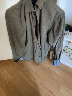 Grön skjorta från Morgan - Skjorta med lång ärm och krage. Försluts med knappar framtill. En bröstficka finns på vänster sida. Manschetterna har en kontrasterande blå insida. Mycket snygg. Mycket bra skick. Mått kan skicka vid behov.