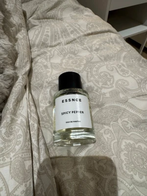 ESSNCE Spicy Pepper Eau de Parfum - ESSNCE Spicy Pepper Eau de Parfum i en stilren, genomskinlig glasflaska med svart lock. Doften har kryddiga toner och flaskan har en minimalistisk vit etikett med svart text. Perfekt för dig som gillar unika och intensiva parfymer. (Endast testad två sprut)
