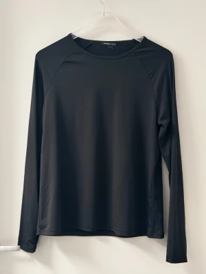 Svart långärmad topp  - Säljer en svart långärmad topp med enkel och stilren design. Tillverkad i ett mjukt och stretchigt syntetmaterial som passar perfekt för träning. Rund halsringning och normal passform. Antal: 4 st 