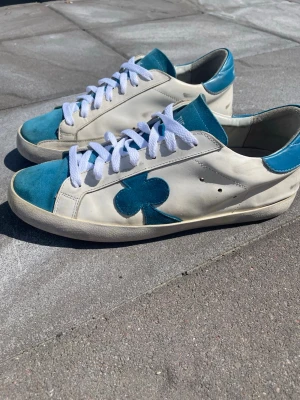 The gallerist skor - Tjena!! Säljer ett par snygga sneakers ifrån the gallerist i vitt och turkost med en unik klöverdetalj på sidan. Skorna har turkosa detaljer på hälen och på tå partiet och även tungan! Vita skosnören som passar perfekt!! Dessa skor är perfekta nu under sommaren och kommer att passa bra till alla sorters tillställningar!! Skicket är 6,8/10 se bilderna! Storlek 42-43!! Hör av dig vid mer frågor eller funderingar🕺mvh Ga🤩