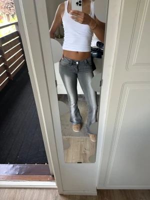 Grå bootcut jeans med låg midja - Säljer ett par grå bootcut jeans med låg midja och klassisk femficksdesign. Jeansen har en snygg tvättad look och sitter tight över låren för att sedan bli vidare nedtill. Perfekta för dig som gillar retrostil och vill ha ett par trendiga jeans. 