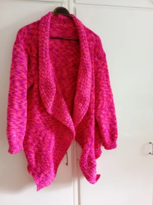 Rosa stickad kofta med sjalkrage XL/XXL - Säljer en färgstark rosa stickad kofta med sjalkrage och avslappnad passform. Koftan har långa ärmar och en snygg melerad effekt i rosa och lila toner. Perfekt för dig som vill ha något mysigt och trendigt att slänga på dig.