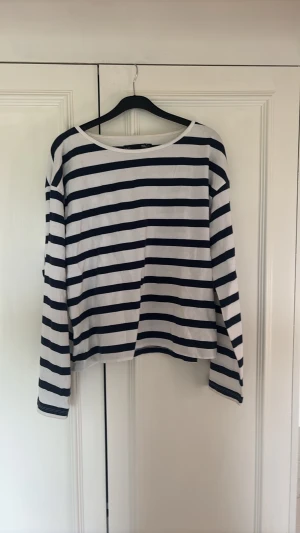 Randig långärmad topp från 157 - Snygg långärmad topp från 157 i vitt och marinblått med klassiskt randigt mönster. Tillverkad i mjuk bomull och har en avslappnad passform med rund halsringning. Perfekt för en chill och stilren look.